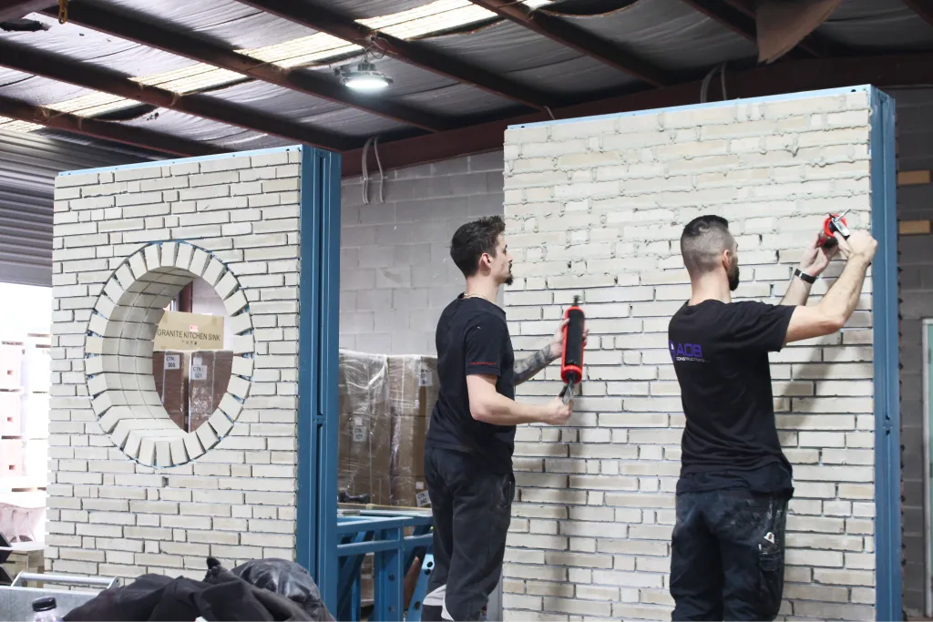 Installers applying sealant with caulking guns to a real brick veneer panel with a cutout